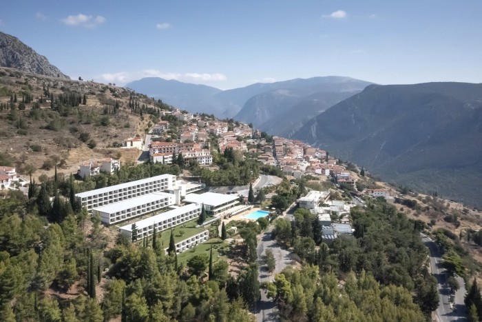 Spectacular white, blocky, rectangular, blocky building set against a dramatic Greek mountains and trees